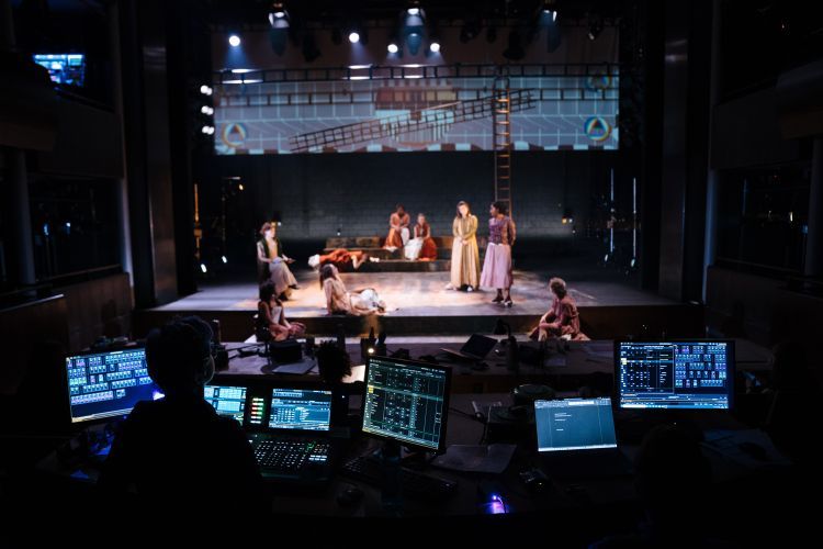 Lighting student working at a lighting desk during a technical rehearsal with the actors on stage